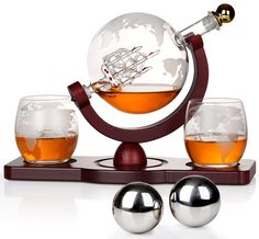 three glasses and a globe on a stand with silver balls around it, all in front of a white background