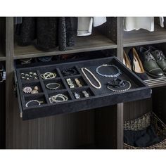 an open drawer with jewelry and shoes on it in front of some clothes hanging from the shelves