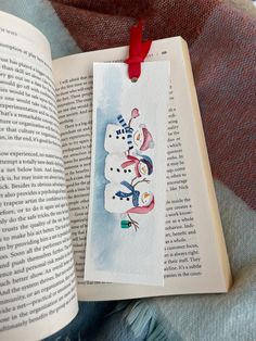 an open book with snowmen on it and a red ribbon hanging from the cover