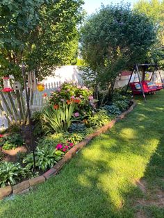 a garden with lots of plants and flowers in it's bed next to a white fence