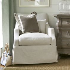 a white chair sitting next to a wooden dresser in a living room under a window