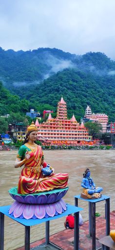 there is a statue sitting on top of a boat in front of some mountains and buildings