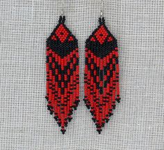 two red and black beaded earrings hanging on a white background, one is made out of