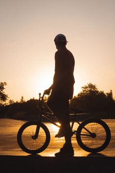 a person standing next to a bike with the sun setting in the back ground behind them