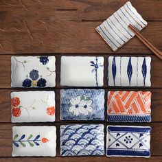 six square plates with different designs and chopsticks next to each other on a wooden surface