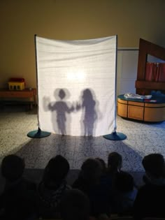 the shadow of two children holding hands in front of a white screen with people on it