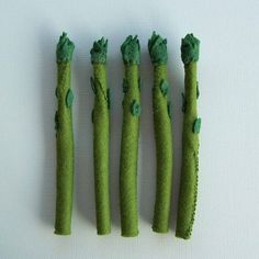 four pieces of green grass with leaves on them and one piece cut out to look like asparagus