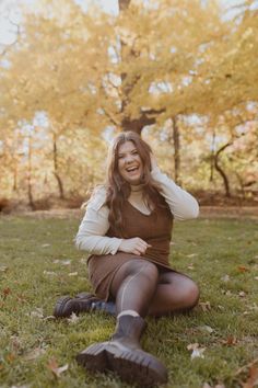 a woman sitting in the grass with her hands on her head and smiling at the camera