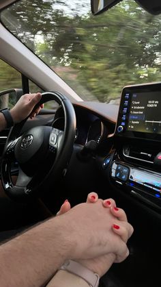 a man driving a car with his hands on the steering wheel while another woman holds her hand