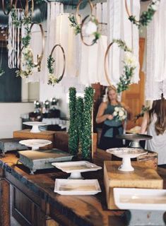 a woman standing in front of a table with flowers and greenery hanging from it