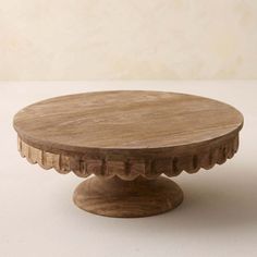 a round wooden table with scalloped edges on a white surface, against a beige background