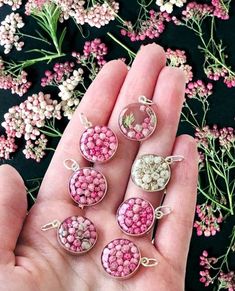 four pink and white beads are in the palm of someone's hand next to some flowers