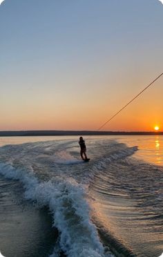 a person on a surfboard being pulled by a boat in the ocean at sunset