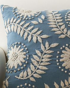 a white couch with a blue pillow on it's back and an embroidered leaf design