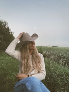 a woman sitting in the grass wearing a cowboy hat