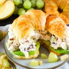 a chicken salad sandwich cut in half on a plate with grapes, apples and croissants