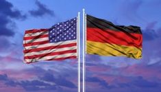 two american and german flags flying side by side in front of a cloudy blue sky