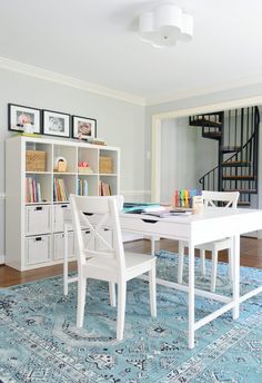 a dining room table with chairs and bookshelf in front of the stairs leading up to the second floor