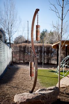 a metal wind chime in the middle of a yard with rocks and trees behind it