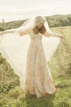 a woman in a wedding dress holding her veil over her head while standing in a field