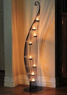 a metal sculpture with candles in it on a wooden floor next to a white wall