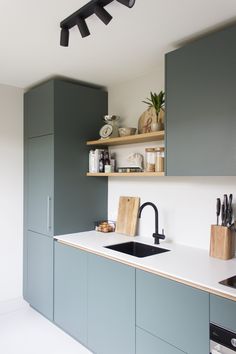 a kitchen with blue cabinets and white counter tops, black faucet, wooden cutting board