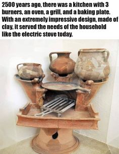 an old fashioned stove with pots and pans on it's stand, in front of a white wall