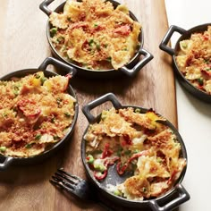 four cast iron pans filled with food on top of a wooden cutting board next to utensils