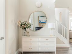 a white dresser with flowers and a mirror on it in a room that has stairs leading up to the second floor