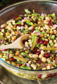 a glass bowl filled with corn, beans and green onions next to a wooden spoon