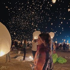 a woman standing in front of many lit up hot air balloons that are floating in the sky