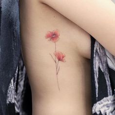 a woman's lower back tattoo with red flowers on her left side ribcage