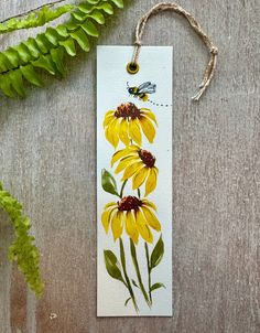 a bookmark with yellow flowers and a bee on it next to a fern plant