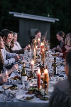 a group of people sitting around a dinner table with candles on the plates and wine bottles in front of them