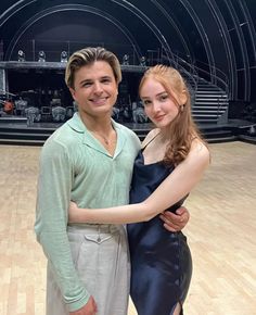 a man and woman standing next to each other in front of a wooden floor with an empty stage behind them