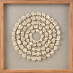 a white beaded necklace in a wooden frame on a gray background with a shadow box underneath it