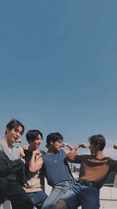 four young men posing for the camera with one pointing at something in the sky behind them