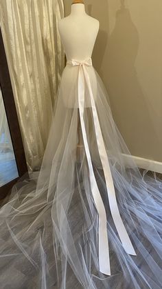 a white wedding dress on display in front of a window with sheer tulle and ribbon