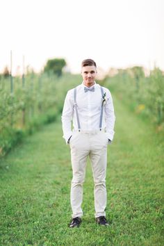 a man standing in the middle of a field wearing suspenders and a bow tie