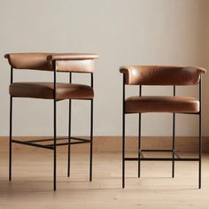 two brown leather chairs sitting on top of a hard wood floor next to each other