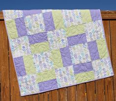 a purple and green quilt hanging on a wooden fence