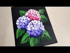 some flowers are painted on a piece of black paper with green leaves and pink and blue flowers