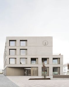 the building has many windows on it and is made of white concrete with a clock at the top