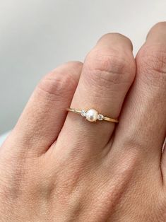 a woman's hand wearing a gold ring with two pearls on the middle finger