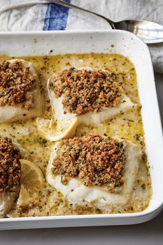 four fish fillets in a white casserole dish with lemon slices and parsley