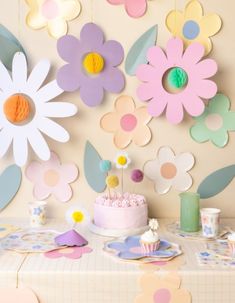 a table topped with a cake covered in frosting next to paper cut outs and flowers