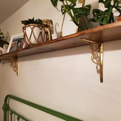 some plants are sitting on top of a wooden shelf above a green metal bed frame