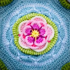 a crocheted flower on top of a blue and green doily in the shape of a circle