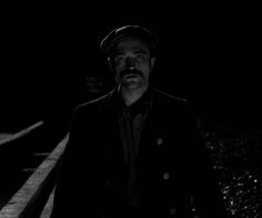 a man standing in the dark wearing a hat