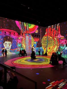 people are sitting on the floor in front of an art installation with colorful images projected on it